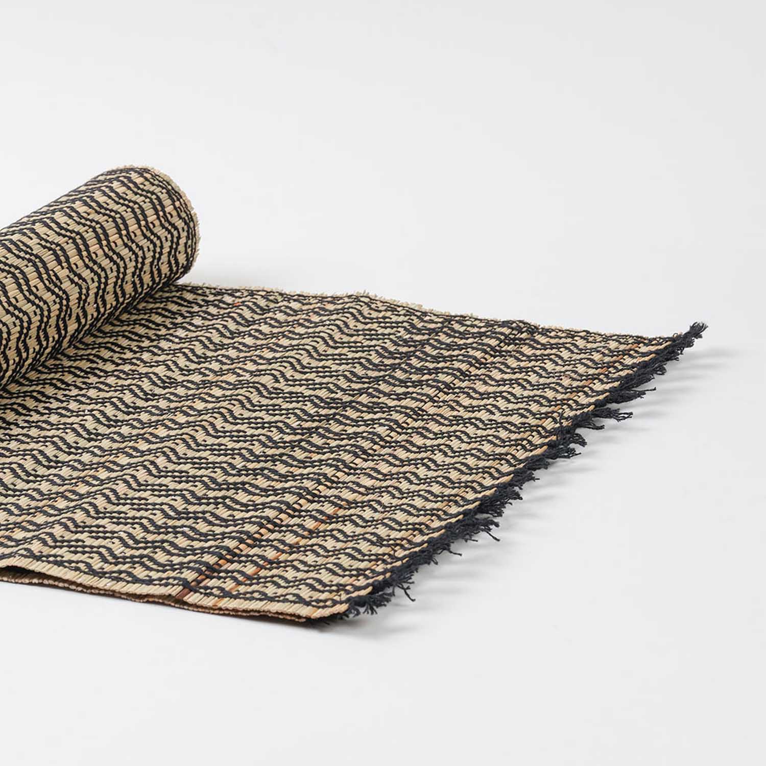 Angled view of a handmade Madurkathi table runner highlighting flexible natural fibre weaving, geometric patterns, and fringe accents