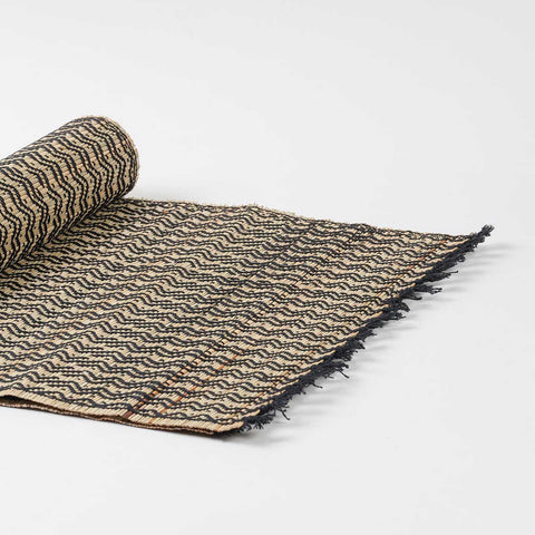Angled view of a handmade Madurkathi table runner highlighting flexible natural fibre weaving, geometric patterns, and fringe accents