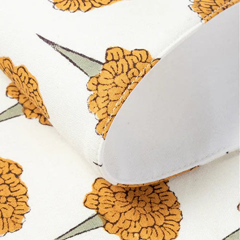 Close-up detail of a white cotton table placemat showing a yellow marigold flower block-print design with a neat stitched edge lining.