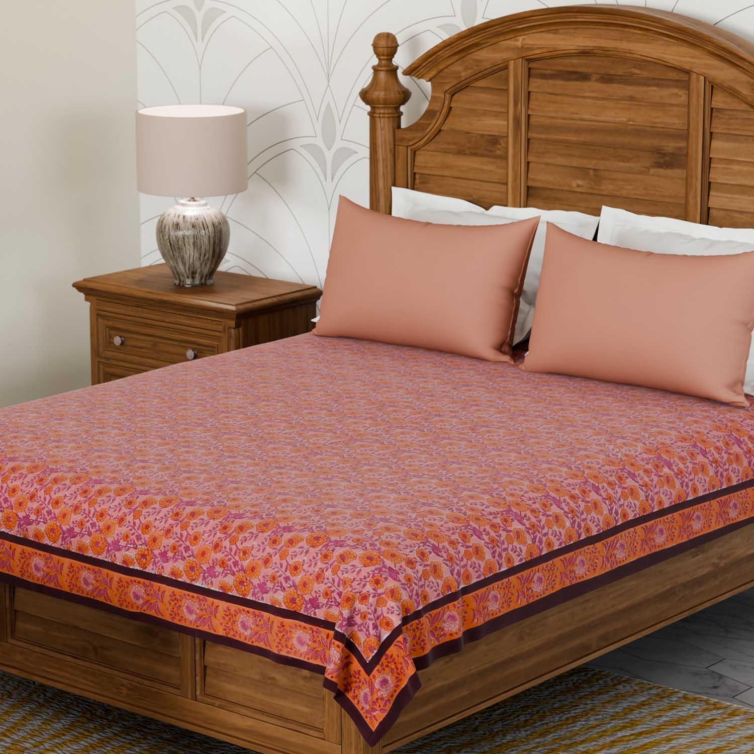 Marigold jaal pink block printed bedcover styled on a bed with coordinated cushions, creating a warm and inviting bedroom setting