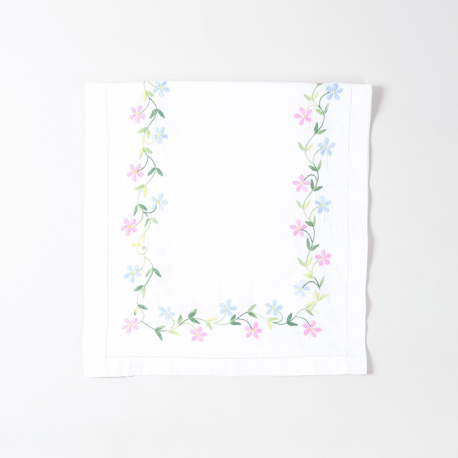 Folded white cotton table runner showcasing colourful daisy embroidery and handcrafted Bengal chikankari detailing