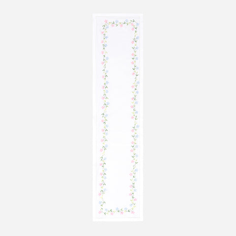 Full-length embroidered table runner featuring multicoloured daisy motifs on a white cotton base displayed on a plain background