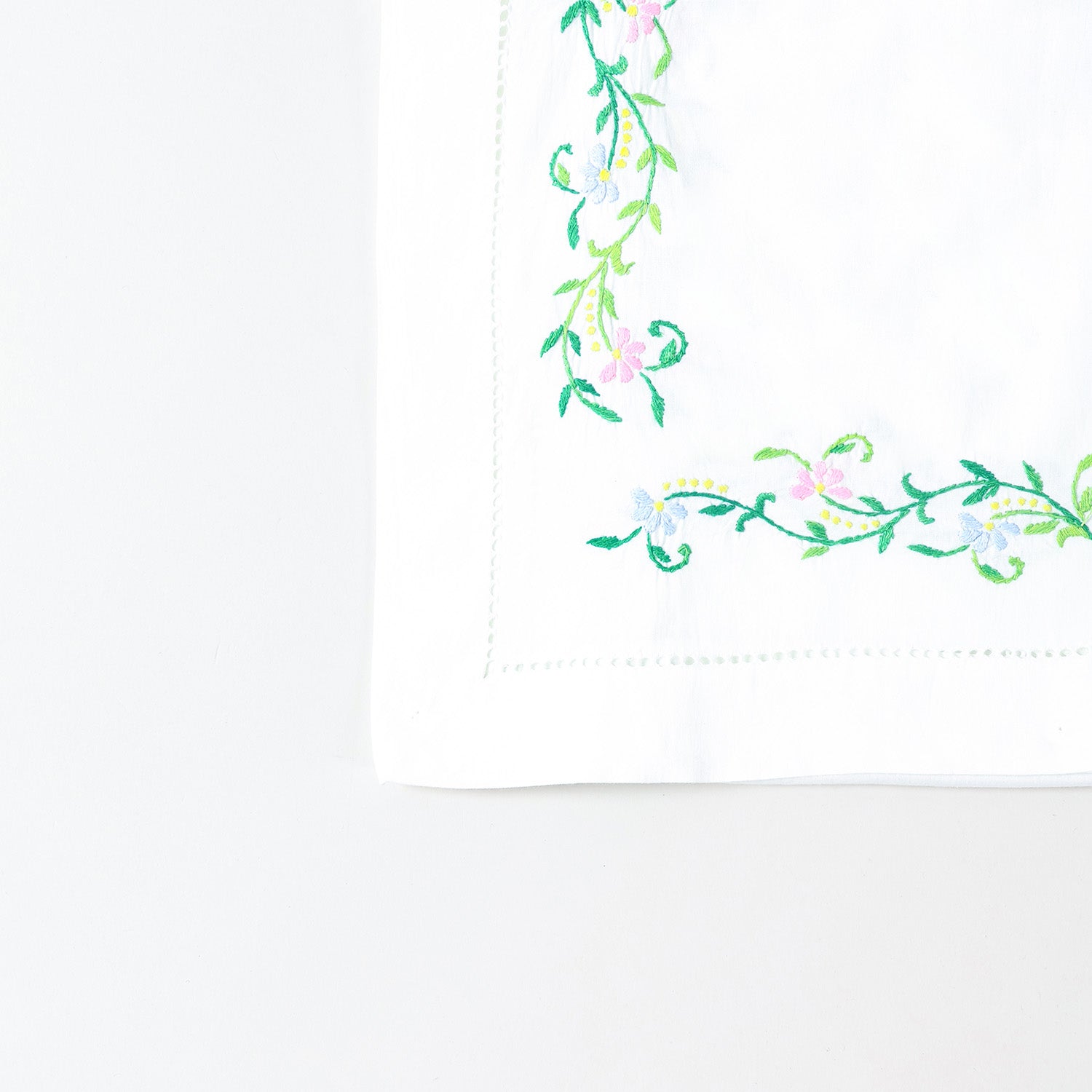 Detailed corner view of a handcrafted embroidered table runner featuring colourful floral vines along the border