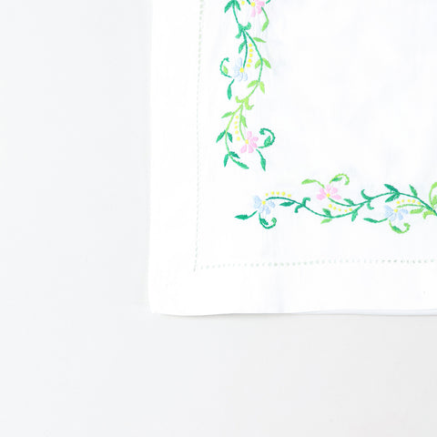 Detailed corner view of a handcrafted embroidered table runner featuring colourful floral vines along the border