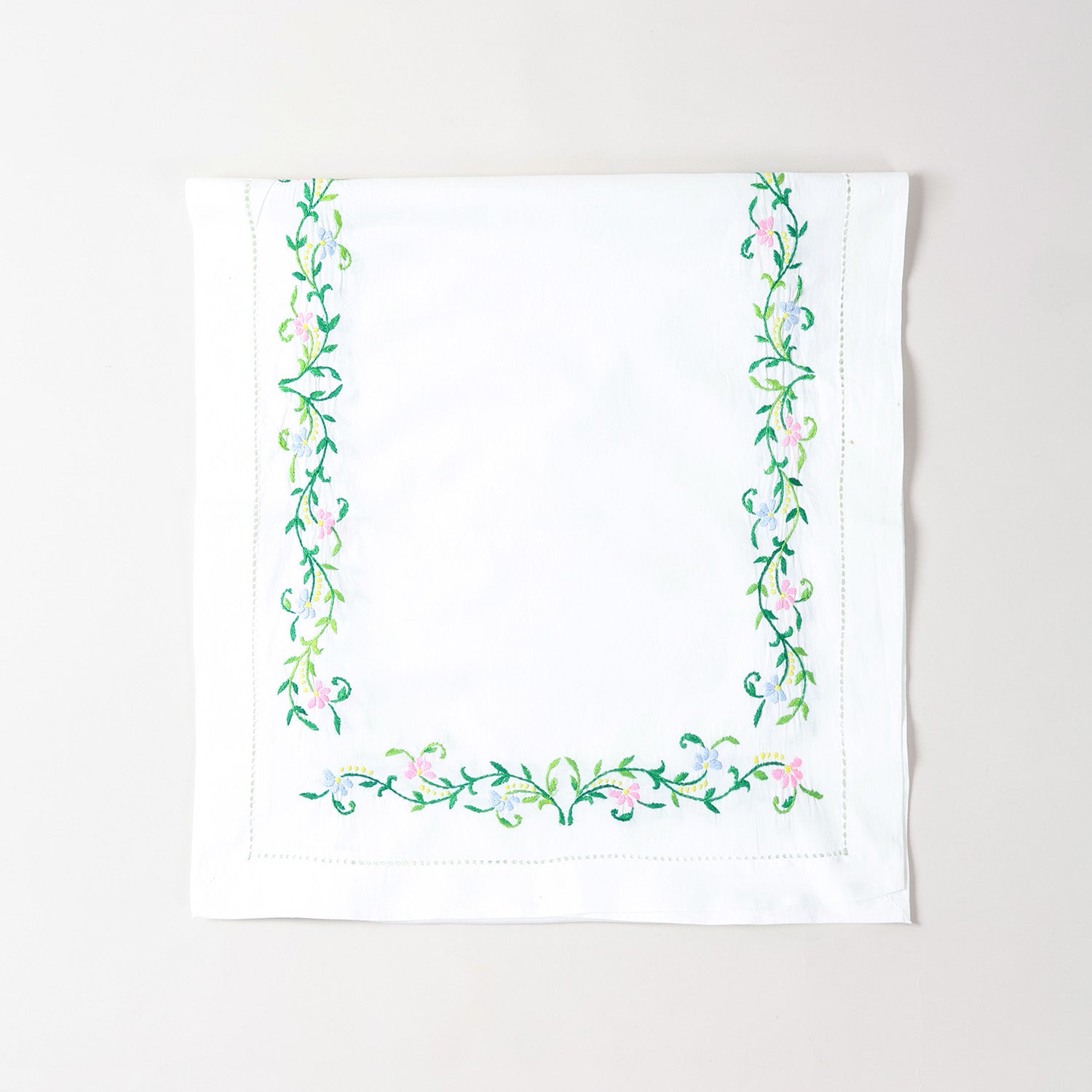 Folded Bengal chikankari runner showcasing multicoloured floral embroidery on soft white cotton table linen