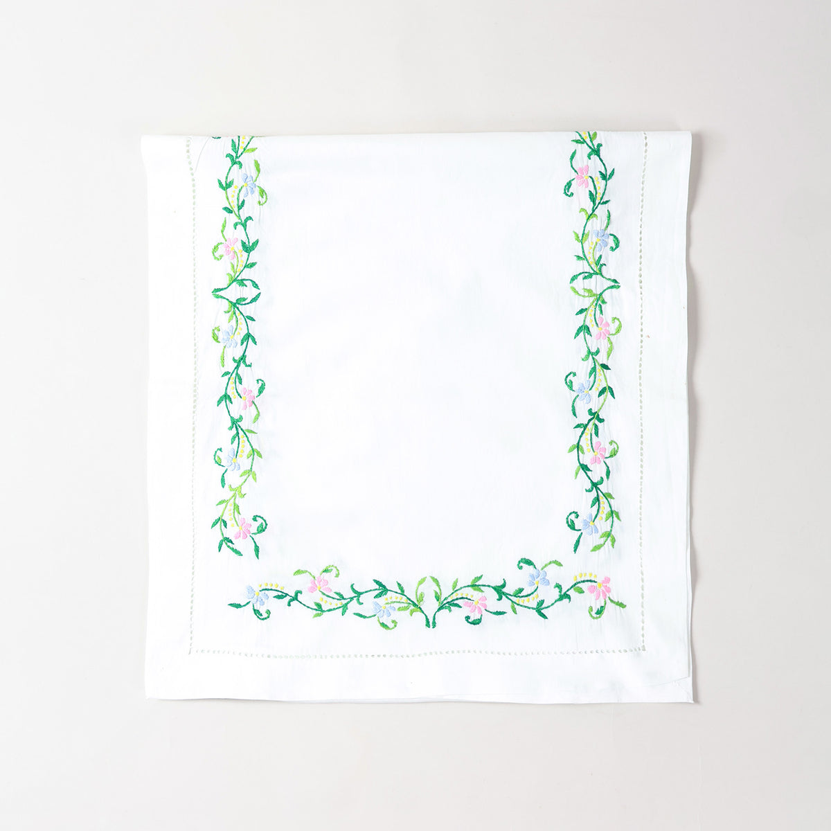 Folded Bengal chikankari runner showcasing multicoloured floral embroidery on soft white cotton table linen