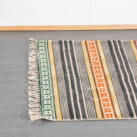 Top view of a multicolor cotton dhurrie rug highlighting geometric stripe block prints and woven fringe detailing