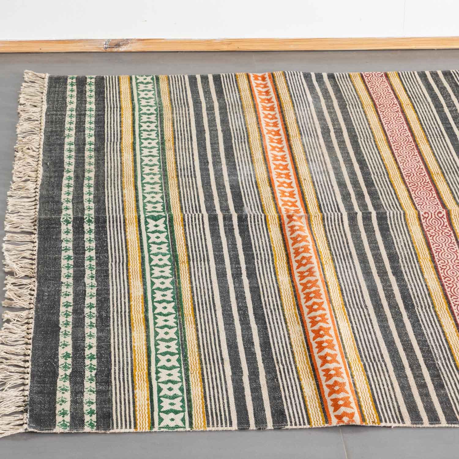 High-angled view of a multicolored cotton rug featuring geometric stripes finished with a cream-colored fringe