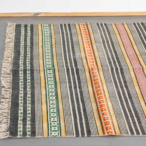 High-angled view of a multicolored cotton rug featuring geometric stripes finished with a cream-colored fringe