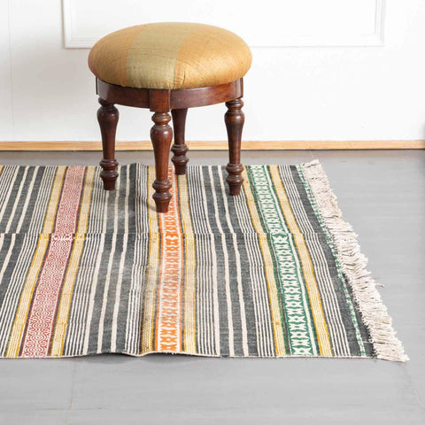 Multicolor handloom cotton dhurrie with geometric stripe patterns styled in a room as a vibrant floor accent