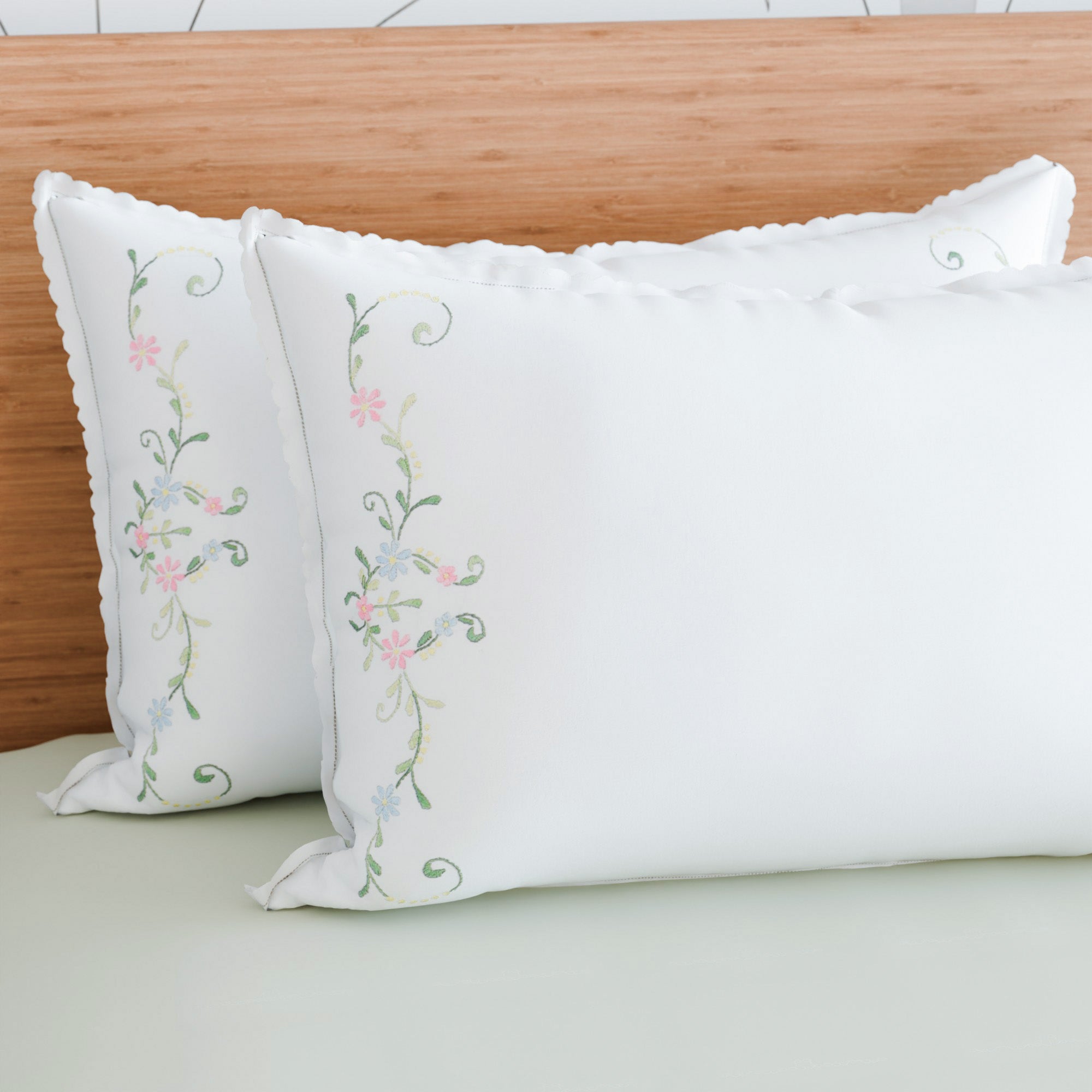 Multi-coloured floral embroidered pillow cases styled on a bed adding soft colour and handcrafted elegance to bedroom decor