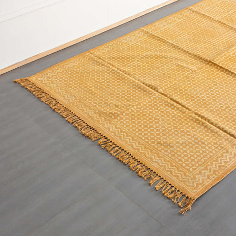 Oblique high-angle view of a mustard cotton dhurrie showcasing geometric block print motifs and handloom texture