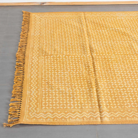 Top view of a mustard handloom cotton dhurrie featuring geometric block print patterns and decorative fringe detailing