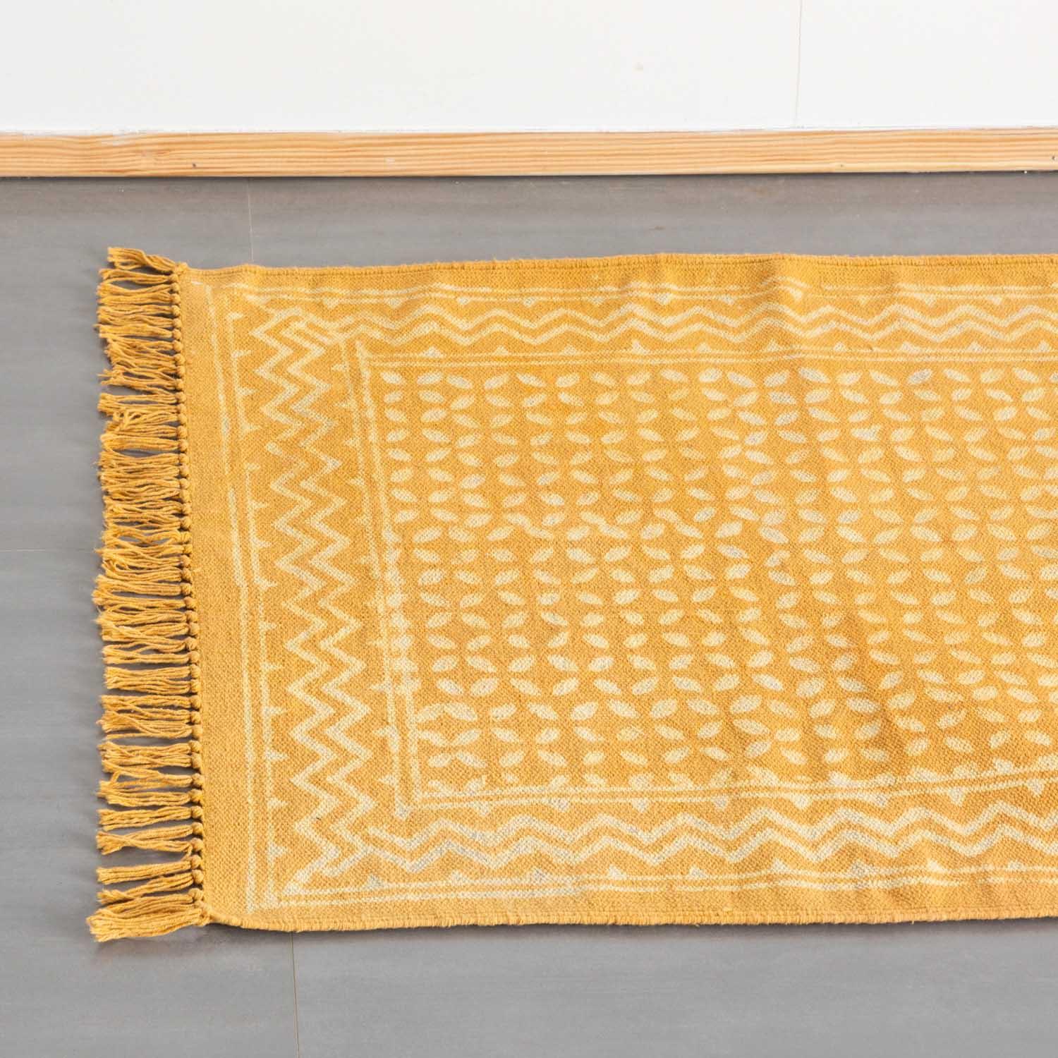 Top view of geometric block print dhurrie rug  in mustard colour with handwoven texture styled on the floor