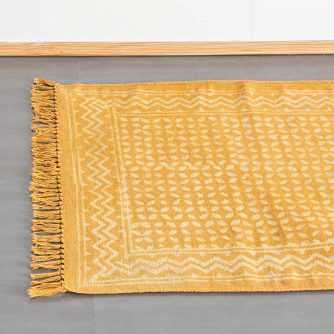 Top view of geometric block print dhurrie rug  in mustard colour with handwoven texture styled on the floor