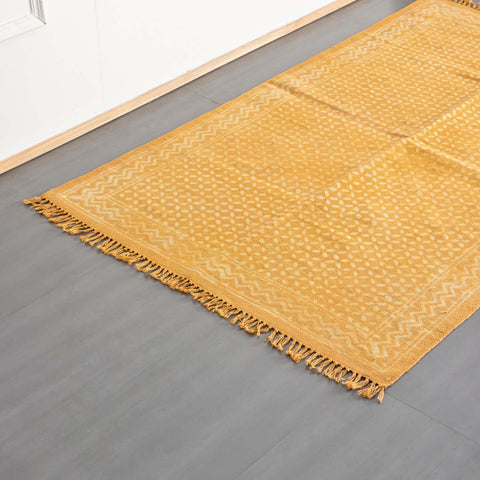Oblique high-angle view of a mustard geometric block printed dhurrie rug showcasing pattern placement and craftsmanship