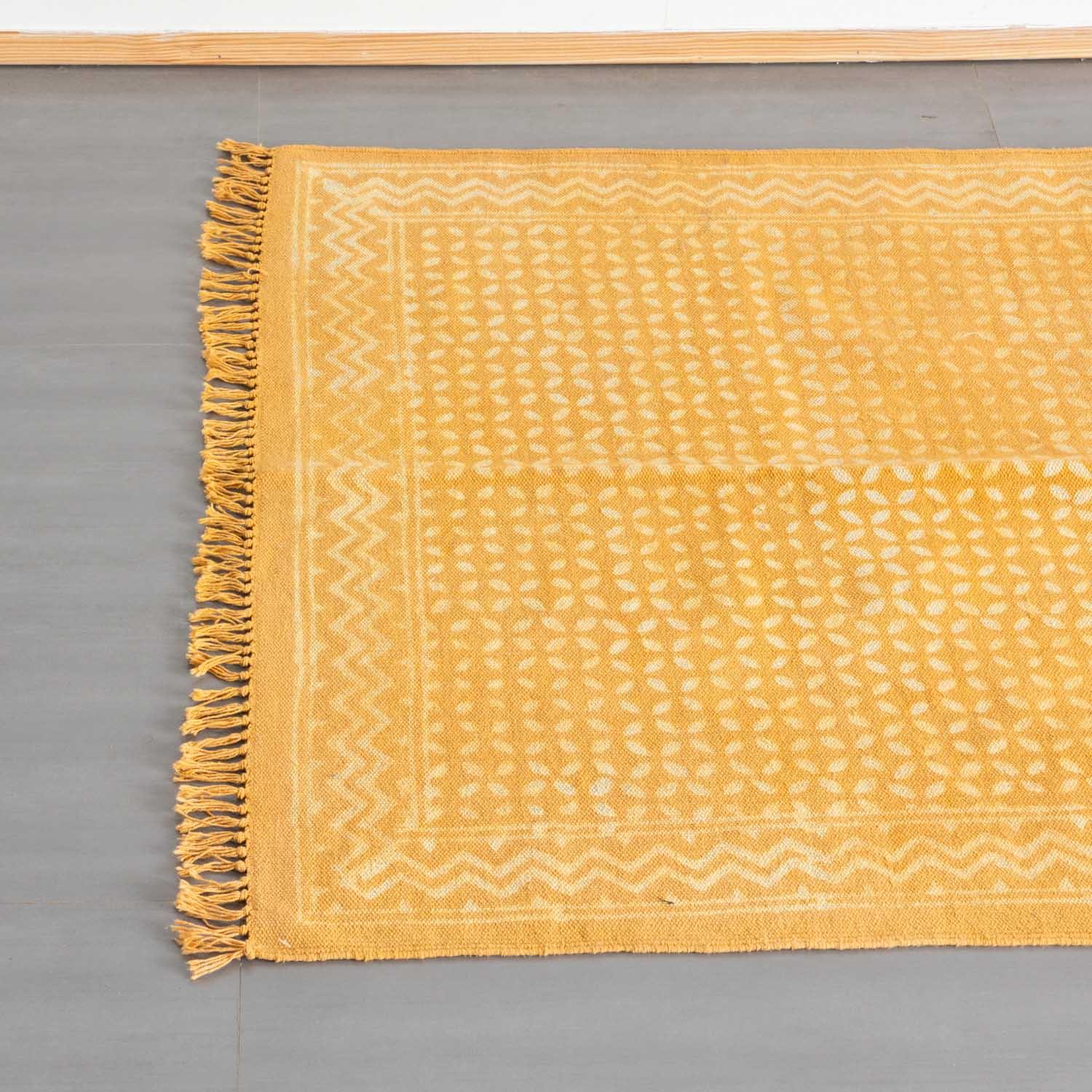 Top view of a mustard cotton dhurrie rug, highlighting geometric block prints and woven fringe detailing