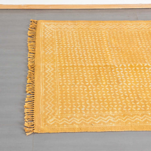 Top view of a mustard cotton dhurrie rug, highlighting geometric block prints and woven fringe detailing