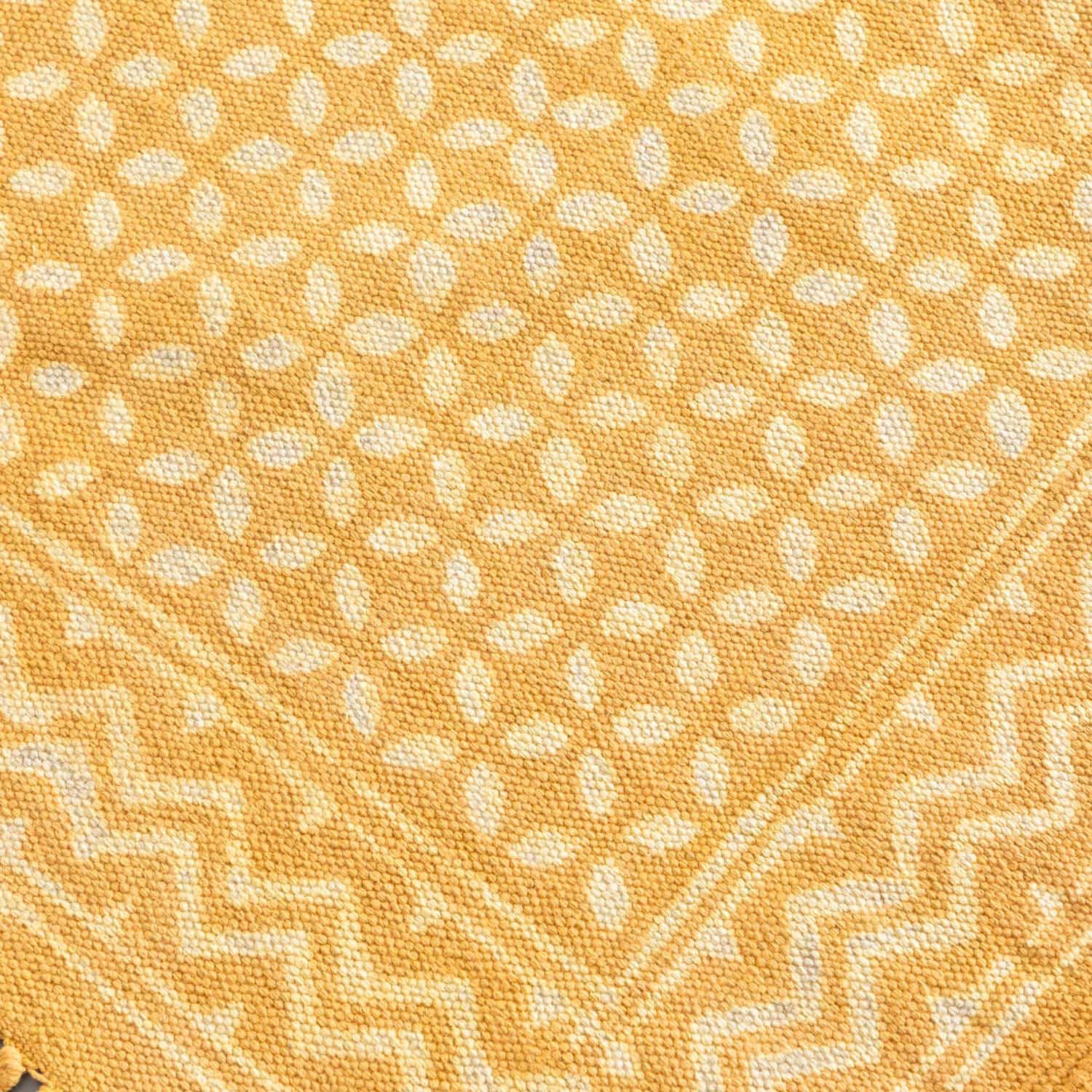 Close-up of geometric block print motifs and textured cotton weave on a mustard handloom dhurrie