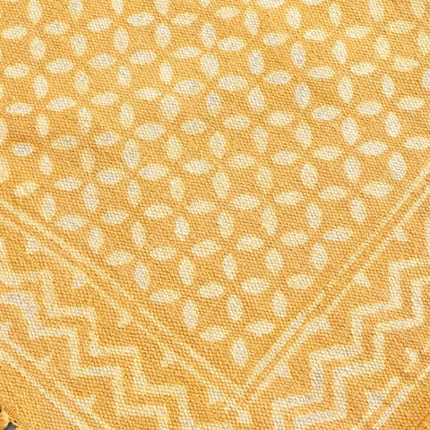 Close-up of geometric block print motifs and textured cotton weave on a mustard handloom dhurrie