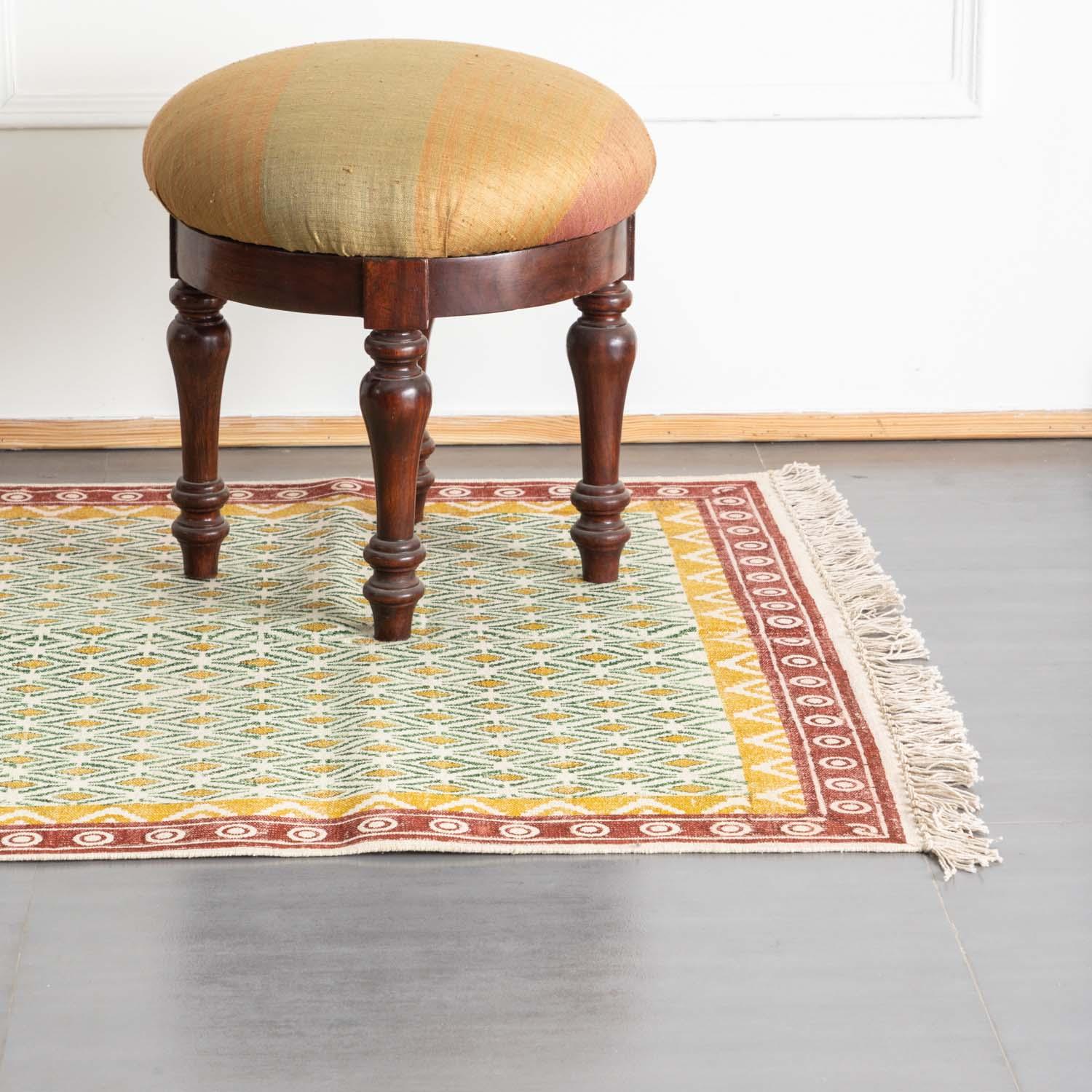 Handmade mustard and red geometric dhurrie rug styled in a reading corner, showcasing traditional weaving and block printing artistry
