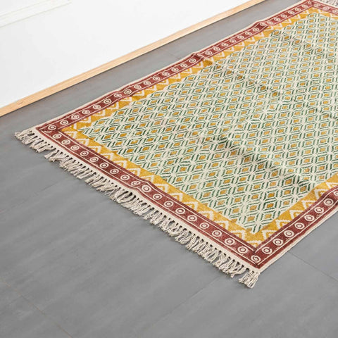 Oblique high-angle view of a mustard and red geometric block printed dhurrie rug showcasing pattern placement and craftsmanship