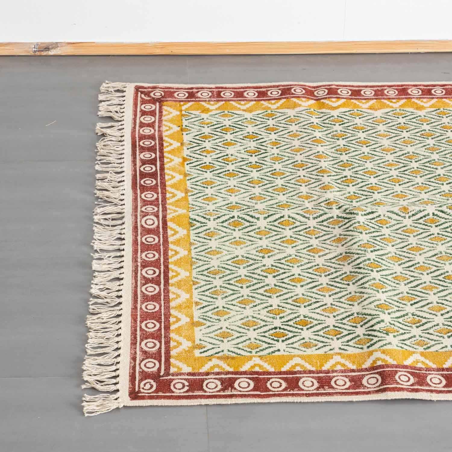 Top view of a mustard and red cotton dhurrie rug, highlighting geometric block prints and woven fringe detailing