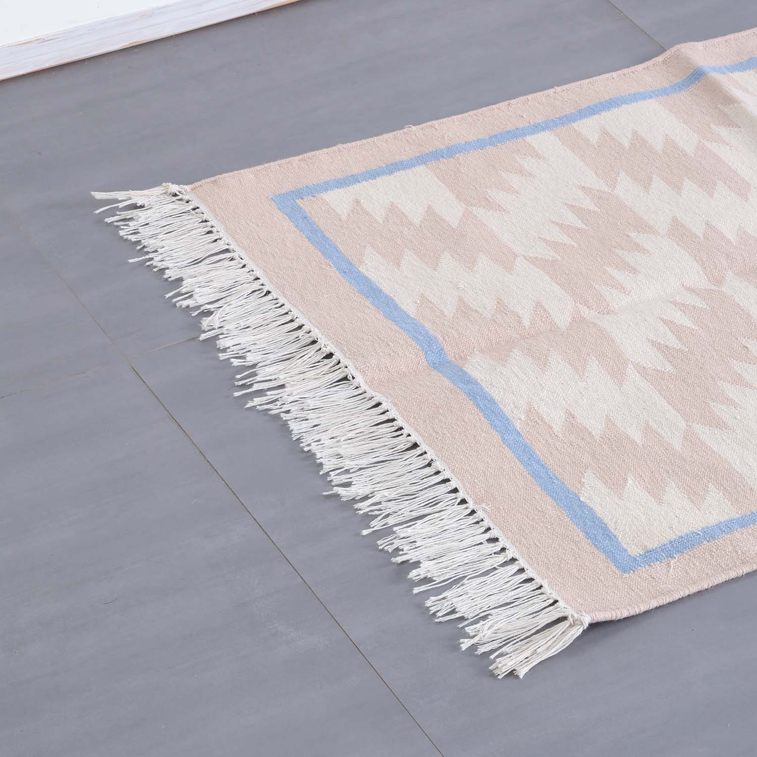 Detailed corner view of a geometric cotton dhurrie highlighting intricate weaving and neutral colour tones