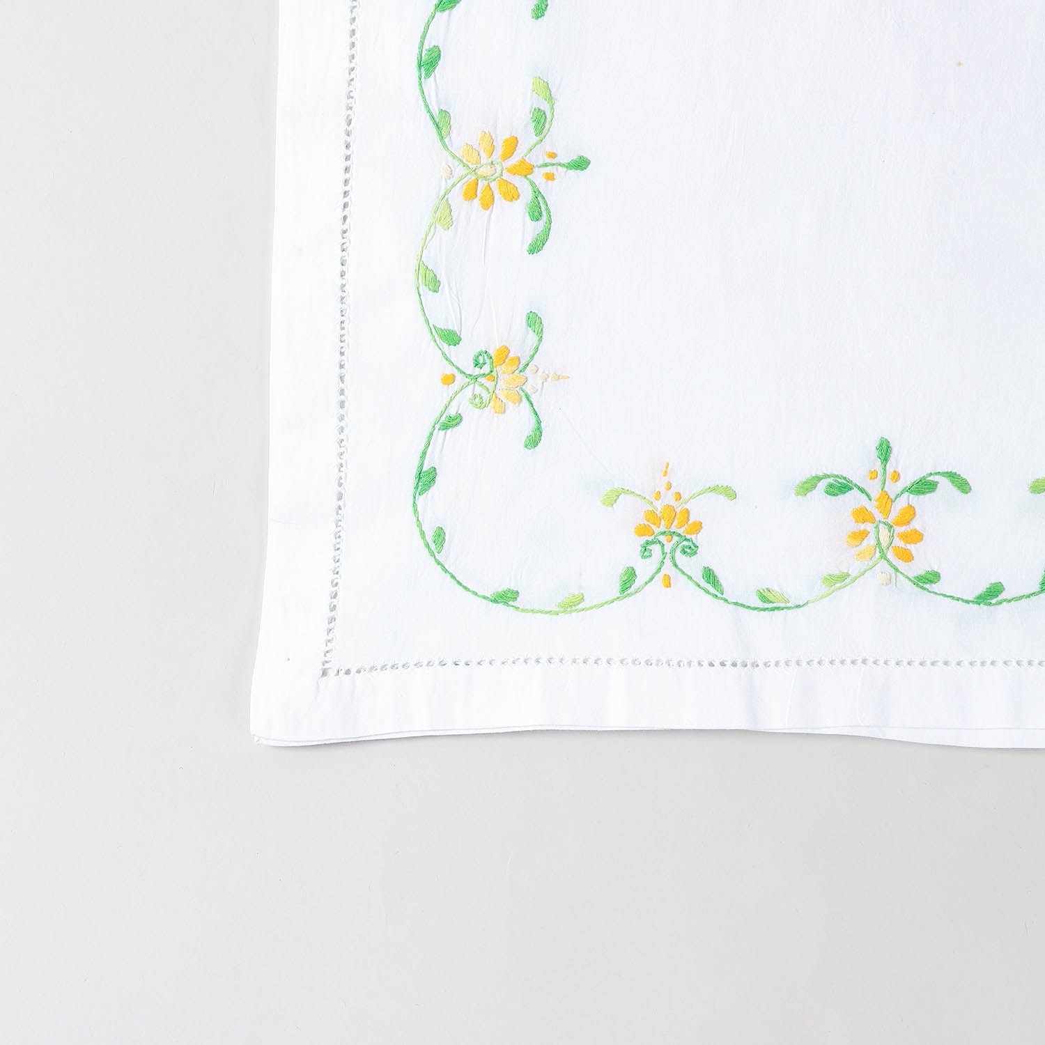  Detailed corner view of a handcrafted table runner featuring orange and green floral vine embroidery along the border