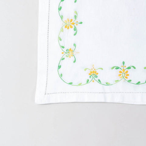  Detailed corner view of a handcrafted table runner featuring orange and green floral vine embroidery along the border
