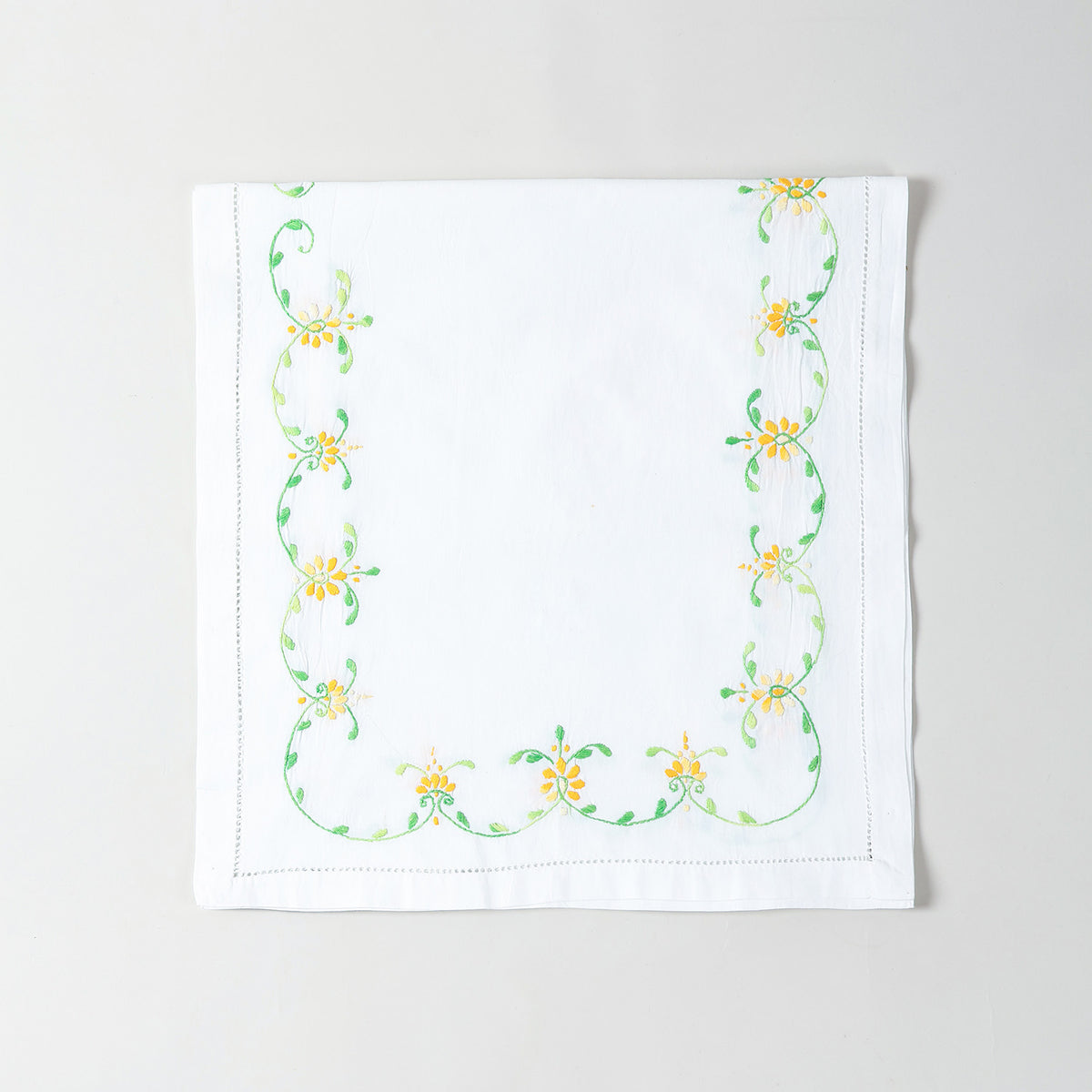 Folded white cotton table runner showcasing orange and green floral embroidery and handcrafted Bengal chikankari detailing