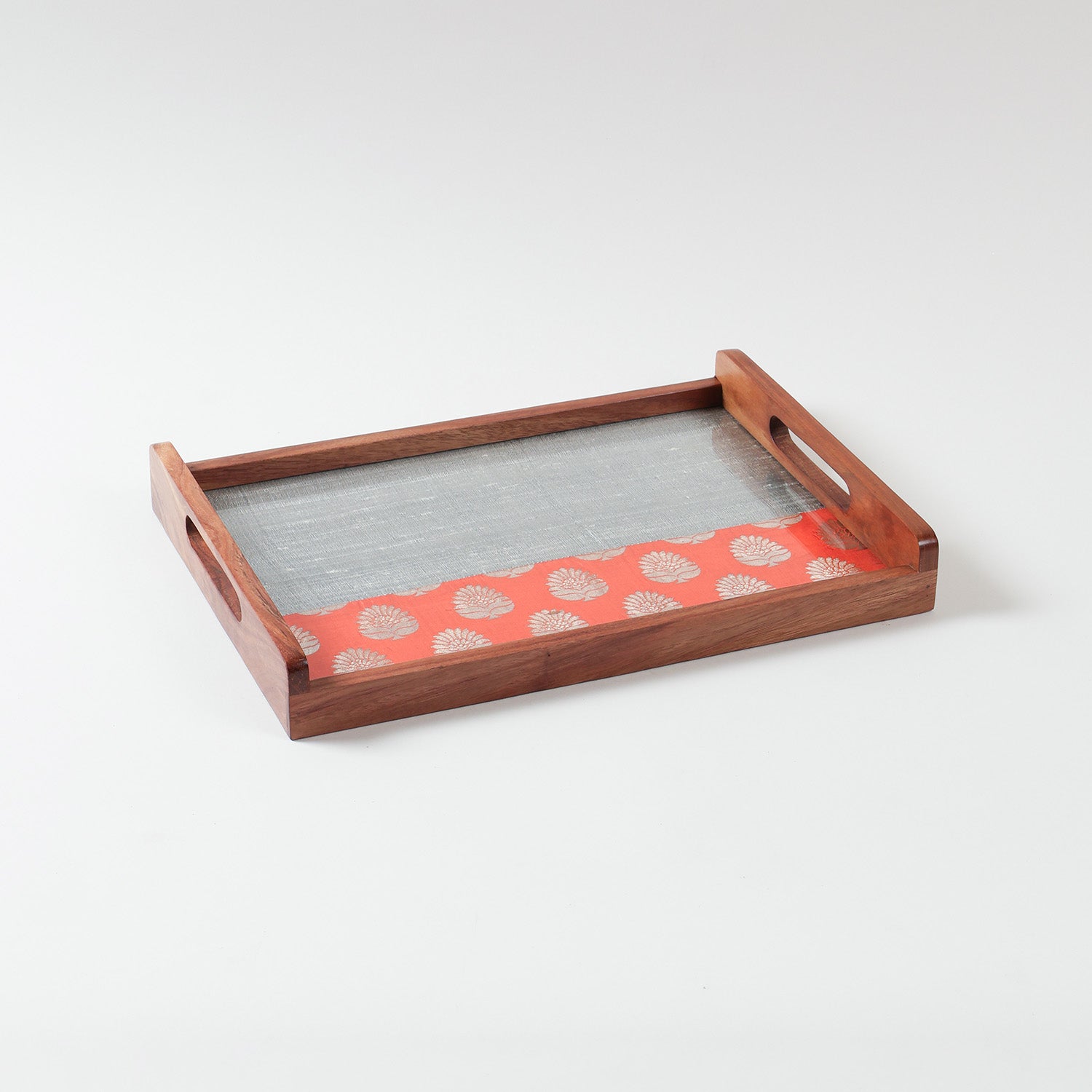 Angled view of handcrafted wooden tray showing dual-tone chanderi fabric in orange and grey with golden paisley motifs under glass