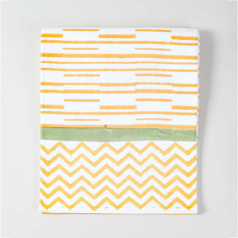 Folded cotton table runner featuring orange striped block print with decorative green border accents