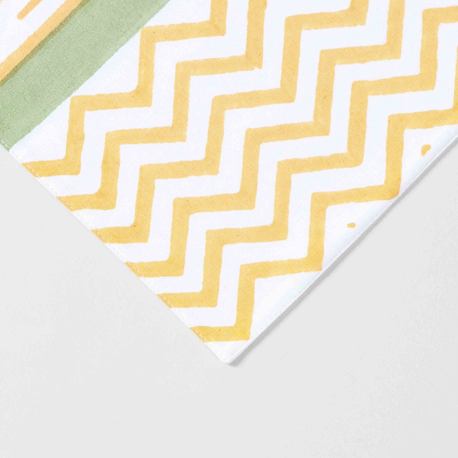 Close-up of orange line motifs green side panels and yellow zigzag border on cotton table runne