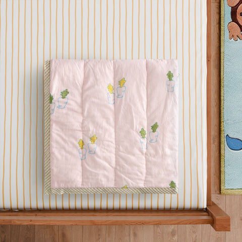 Styled close-up of a hand block printed cotton quilt featuring pastel bunny and carrot motifs, showcasing artisan craftsmanship and soft texture