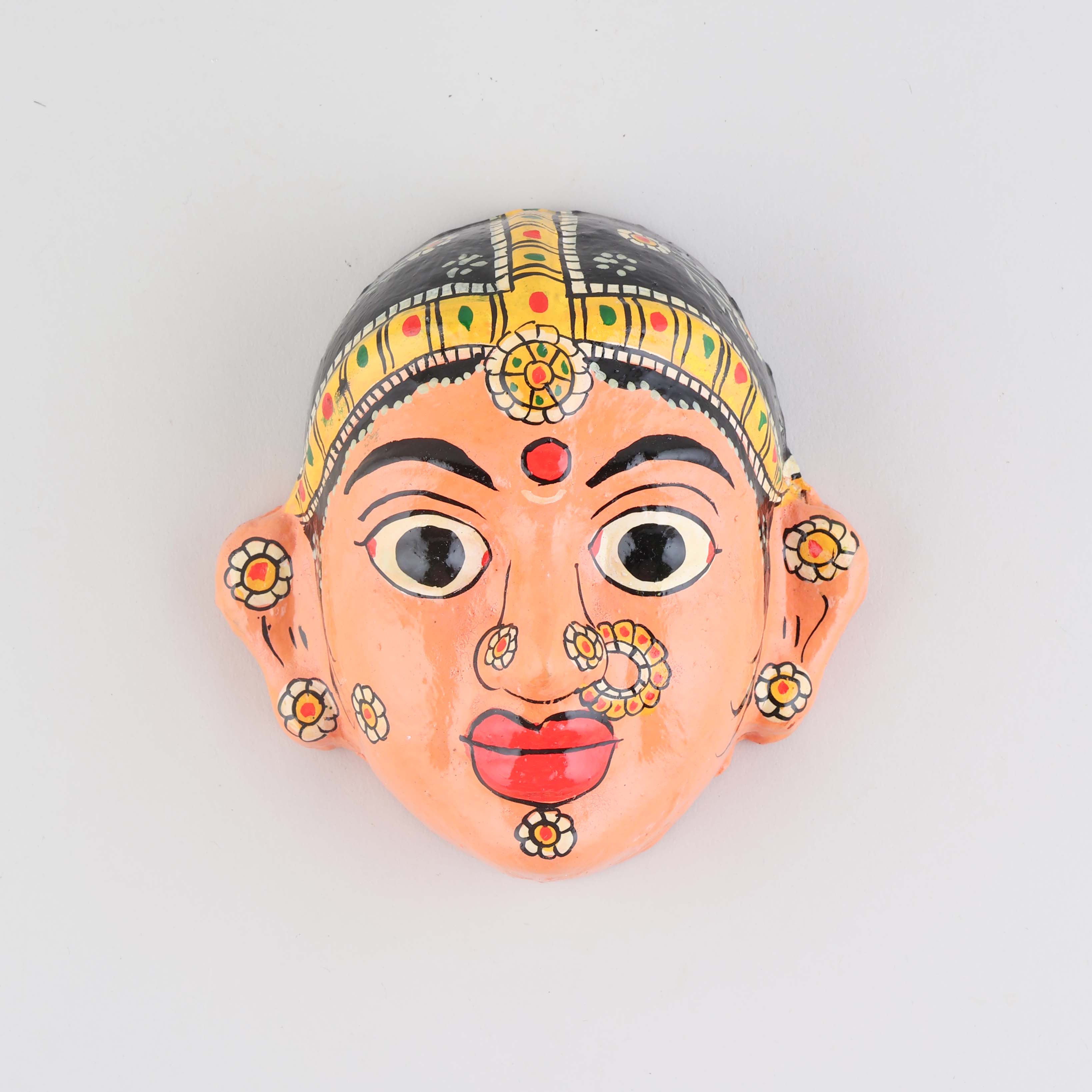 Hand-painted peach Cheriyal female mask crafted from papier-mache, featuring intricate folk art detailing and traditional craftsmanship on a plain background