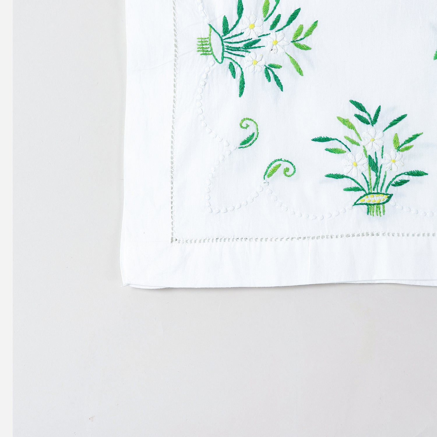 Detailed corner view of a handcrafted table runner featuring elegant periwinkle-inspired floral embroidery along the border