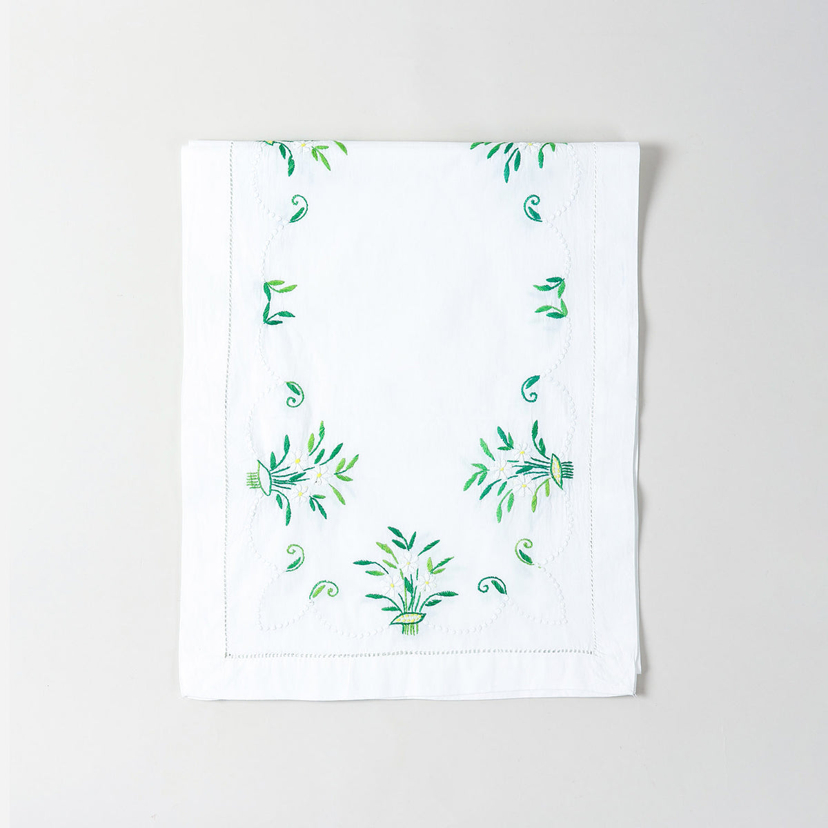 Folded white cotton table runner showcasing delicate periwinkle-inspired floral embroidery and handcrafted Bengal chikankari detailing