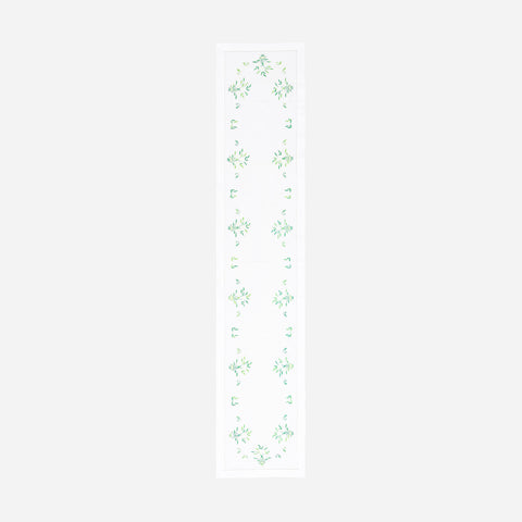 Full-length embroidered table runner featuring white and green floral motifs inspired by periwinkle blooms on a white cotton base, displayed on a plain background 