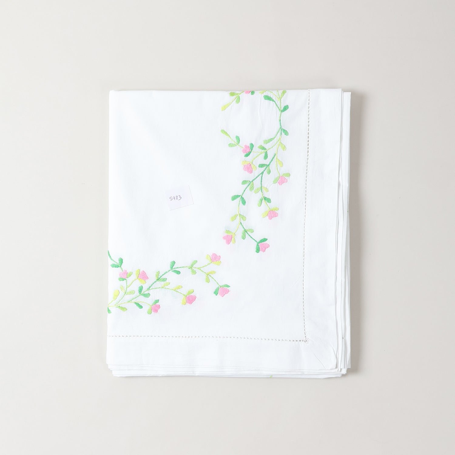 Corner view of embroidered cutwork table cloth featuring pink floral motifs on a white cotton base