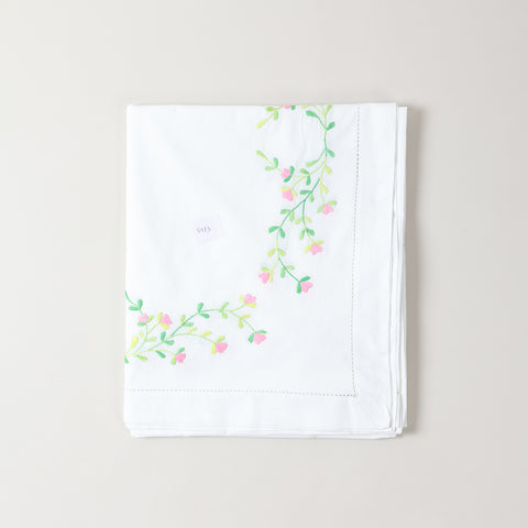 Corner view of embroidered cutwork table cloth featuring pink floral motifs on a white cotton base