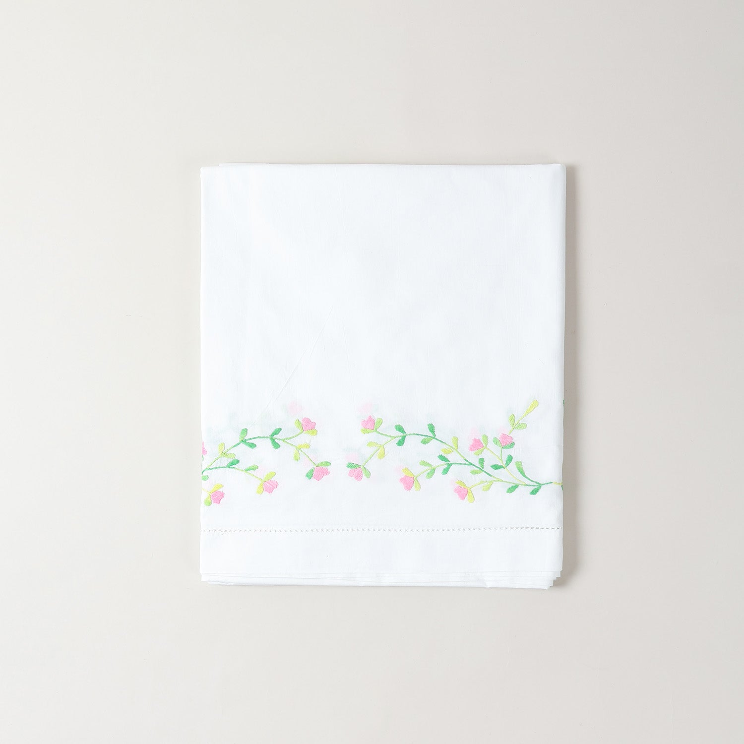 Folded embroidered cotton table cloth showcasing pink floral motifs and intricate cutwork craftsmanship