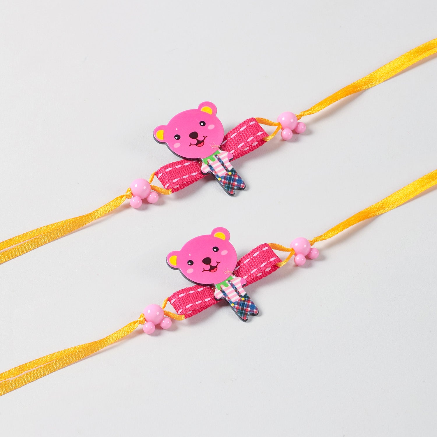 Close-up of the handmade pink cartoon Teddy Bear Wooden Kids Rakhi Set of 2, highlighting the colourful wooden teddy design and yellow ribbon details.