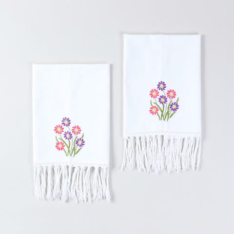 Set of two white cotton kitchen towels featuring pink and purple daisy floral embroidery and tasselled edges