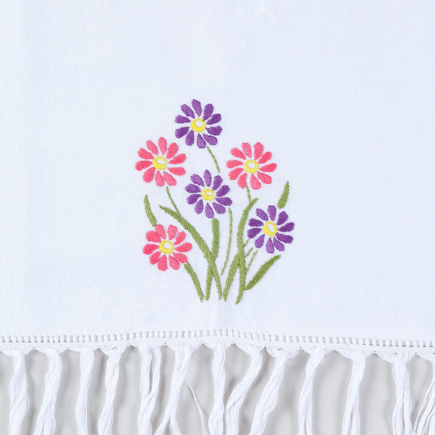 Close-up of pink and purple daisy hand embroidery with textured tassel fringe on cotton kitchen towel