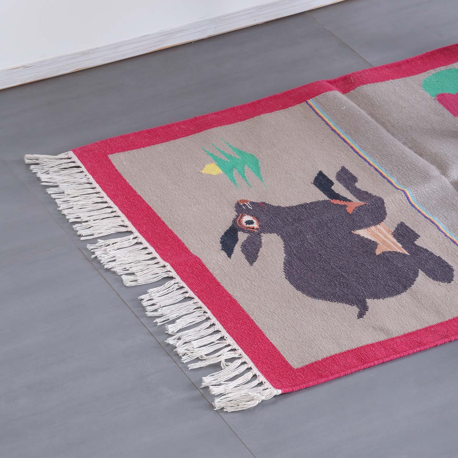 Detailed corner view of a handloom cotton rug featuring peacock and rabbit motifs with textured woven patterns