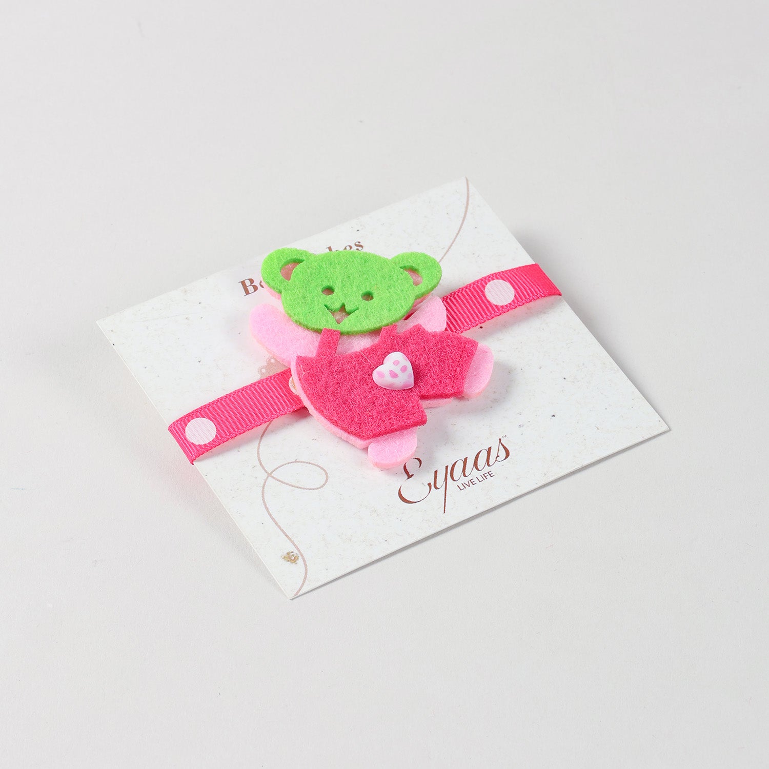 Angled view of the handmade pink Teddy Bear Felt Kids Rakhi attached to a festive Best Wishes card for Raksha Bandhan gifting