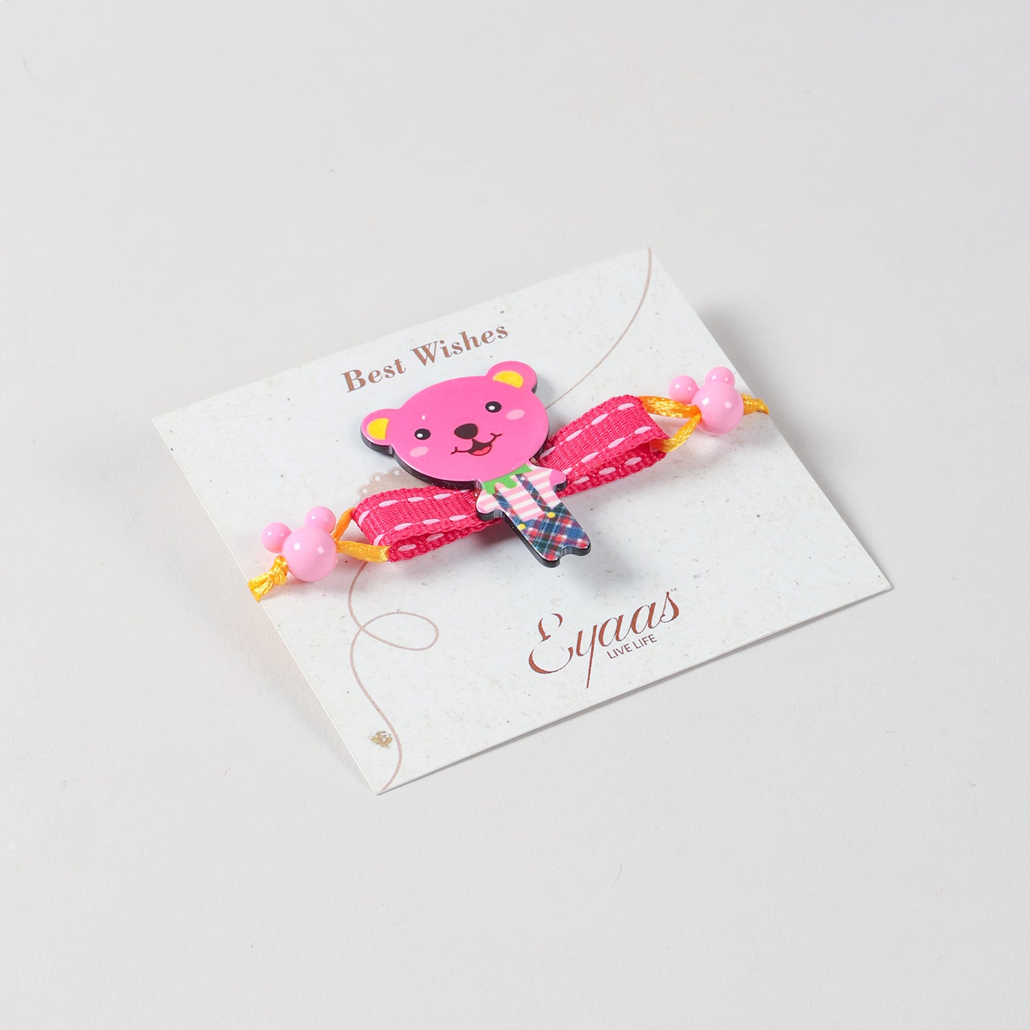 Angled view of the pink Teddy Bear Wooden Kids Rakhi Set of 2 attached to a festive Best Wishes card, ready for Raksha Bandhan gifting