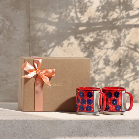 Set of two red ceramic mugs with blue floral hand-painted motifs, styled with a gift box, creating a charming gifting 