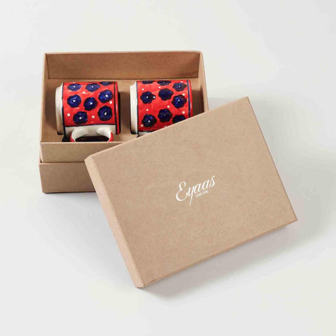 Open gift box displaying two red ceramic mugs with blue floral hand-painted designs ready for gifting